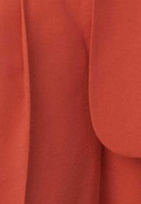 Primo piano di un tessuto rosso piegato con texture liscia e cuciture visibili, che mette in risalto il suo colore ricco e caldo e il materiale morbido.