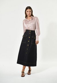 Lunga gonna in denim scuro con bottoni dorati e tasche, abbinata a una blusa in satin rosa chiaro con colletto arricciato e maniche lunghe.