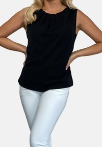 Musta hihaton paita, jossa on laskostettu pääntie, yhdistettynä istuviin valkoisiin housuihin. Kangas on sileä ja siinä on mieto kiilto.