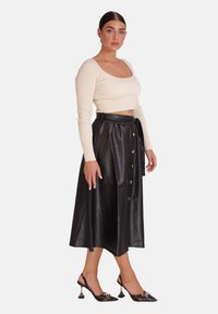 Haut à manches longues côtelé crème associé à une jupe midi en cuir synthétique noire avec une ceinture à nouer et des boutons décoratifs.