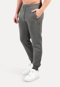 Pantalones deportivos grises hechos de mezcla de algodón, con bolsillos laterales, cintura elástica y puños acanalados, combinados con zapatillas blancas.