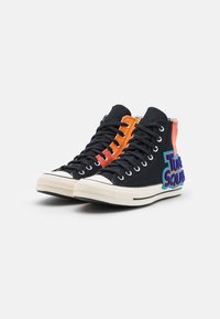 Schwarze Canvas-High-Top-Sneaker mit orange-roten Akzenten, versehen mit strukturierter Stickerei "Tune Squad" an der Seite und weißen Gummisohlen.