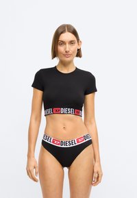 Svart crop-top med korte ermer, med en rød og hvit "DIESEL" logo-bånd. Matchet med svarte høyt midjede undertøy, også med logo-bånd.