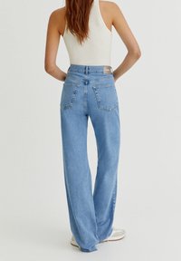 Jean en denim bleu clair à coupe large, avec des poches plaquées et une taille haute. Le tissu a une texture lisse et un design épuré.