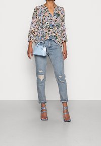 Blouse à manches longues à motif floral dans des couleurs pastel, associée à un jean léger bleu déchiré, un petit sac à main bleu clair et des sandales bleues à lanières.