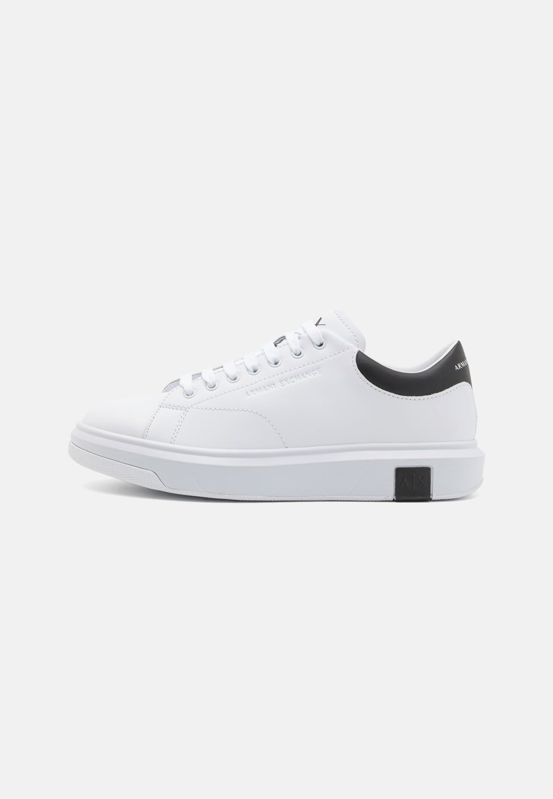 Sneaker bianco con tomaia in sintetico liscia, design a punta rotonda, accentuazione nera nel tallone e chiusura con lacci. Presenta suole testurizzate e un dettaglio con il logo.