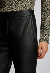 Svarta läderbyxor har en jämn textur och en strömlinjeformad design. En siddragkedja tillför funktionalitet, i kombination med en mönstrad topp.