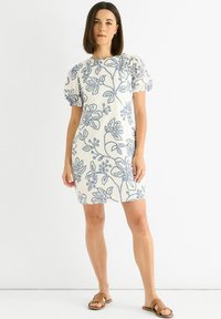 Short-sleeve floral dress in cream with blue embroidered pattern, fitted design, and knee-length cut. Flat sandals complete the look.