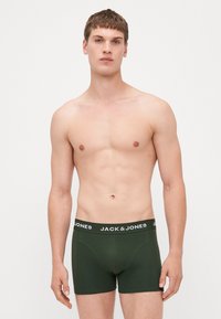 Grüne Baumwoll-Boxershorts mit einem schwarzen Bund, der das Logo "JACK & JONES" trägt. Glatte Textur und enganliegendes Design.