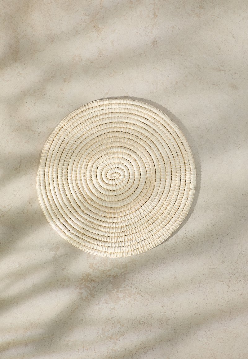 Round placemat woven from natural fibers, featuring a light beige color, smooth texture, and concentric circular pattern.