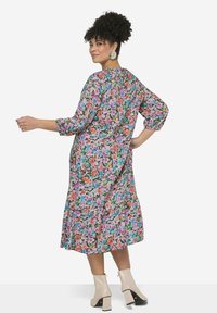 Robe midi florale avec des manches trois-quarts, arborant un motif multicolore sur un fond clair. Portée avec des bottines couleur crème.
