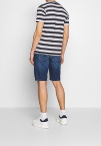 Randig svart- och vit t-shirt tillsammans med blå denimshorts, bärs med vita sneakers med marinblå detaljer och ankelsockor.