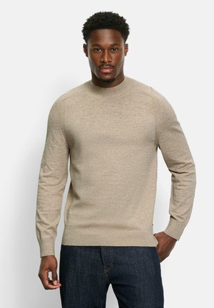 Beiges Rundhals-Sweatshirt mit langen Ärmeln, gerippten Bündchen und Saum, aus einem weichen, strukturierten Stoff. Kombiniert mit dunklen Jeans.