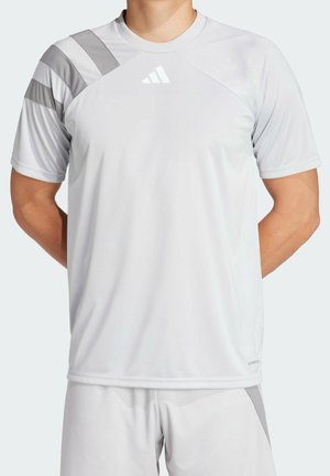 Personne portant un t-shirt de sport gris clair à manches courtes, rayures grises en diagonale sur les épaules et short assorti, bras derrière le dos.