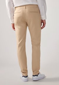 Beige tailored trousers with back pockets, paired with white sneakers featuring blue accents. Smooth texture, classic fit, and clean design.