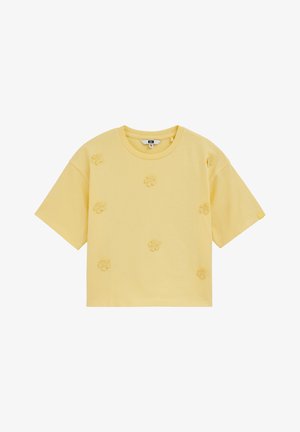 Sárga, rövid ujjú, kerek nyakú póló, amelynek elején és vállain hét kis texturált virágapplikáció egyenletesen elosztva helyezkedik el.