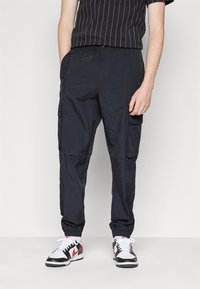 Marinkrabattbyxor i lätt, strukturerad tyg. Har sidofickor, elastiska muddar och en avslappnad passform. Kombineras med en svartrandig t-shirt och sneakers.