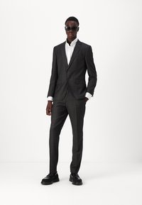 Kulfyret jakkesæt med slim fit, struktureret stof, notched revers, knaplukning, parret med en hvid skjorte og sorte sko.