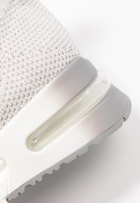 Světle šedá sportovní bota s texturovaným pleteným svrškem, průhlednou vzduchovou polstrovací jednotkou a odolnou gumovou podešví.