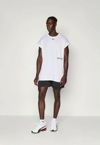 Fehér, rövidujjú, bő szabású póló fekete logóval, fekete sorttal és piros részletekkel ellátott fehér edzőcipővel párosítva.