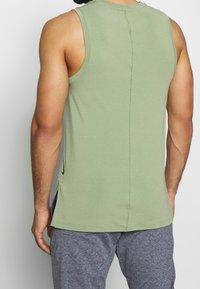 Grön ärmlös tanktop med rak fåll, sidokilar och kontrasterande sidopaneler. Tillverkad av mjukt, lätt material.