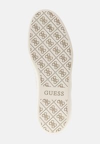 Schuhsohle in Beige mit gemusterter Oberfläche, die ein wiederholtes Logo in einem Rautenmuster zeigt. "GUESS" ist am unteren Rand in der Mitte aufgedruckt.