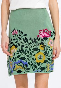 Jupe tricotée verte ornée d'un motif floral avec des fleurs roses, jaunes et bleues. Elle a une coupe ajustée et une texture lisse.