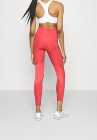 Leggings rouges taille haute en tissu respirant, avec des motifs de panneaux contrastants et un logo à la taille. Texture lisse et forme ajustée.