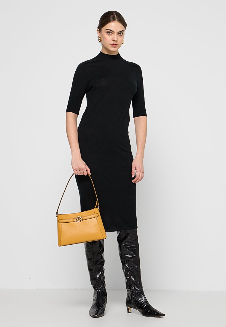 Zwart nauwsluitend jurkje met korte mouwen, gecombineerd met een gele handtas en glanzende zwarte laarzen tot de knie. Glad textuur, minimalistisch ontwerp.