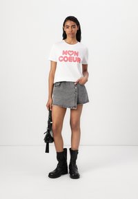 Balta medvilninė marškinėliai su rožiniu tekstu "MON COEUR", derinami su pilku džinsiniu sijonu ir juodais aulinukais. Modelis laiko juodą rankinę.