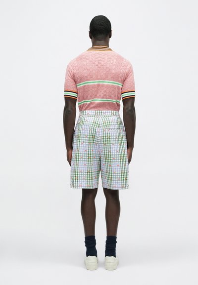 Κόκκινο πόλο με σχέδιο και κοντά μανίκια, με πολύχρωμες ρίγες· σετ με καρό σορτς μήκους μέχρι το γόνατο σε πράσινο και άσπρο χρώμα, με μικρές ανθοκομικές λεπτομέρειες.