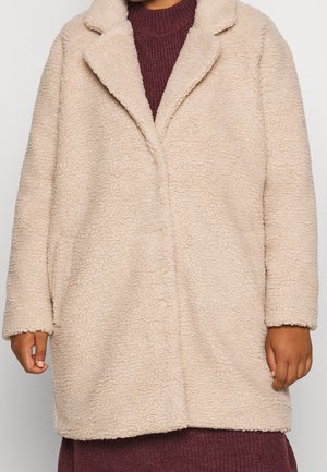 Beige neplederen bontjas met een gestructureerd oppervlak, reverskraag en een ontspannen pasvorm, met lange mouwen en een enkele knoopsluiting.