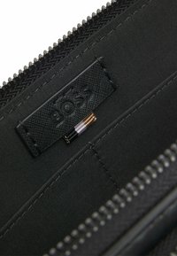 Black fabric interior of a bag with an embossed BOSS label and a tricolor fabric loop inside a zipped compartment.