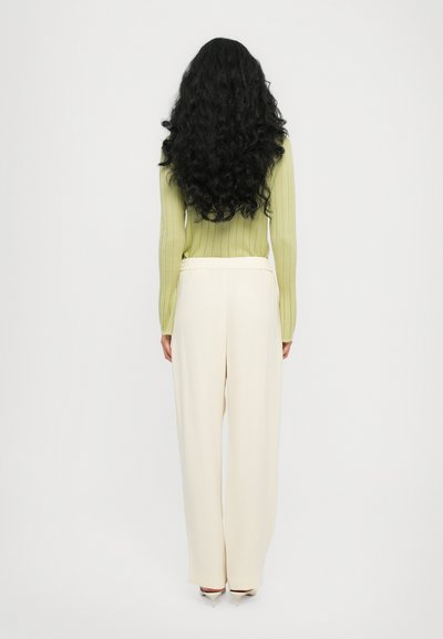 Hellgrüner gerippter Pullover, cremefarbene weite Hose, glatte Textur, elastischer Bund, von hinten betrachtet, lange lockige schwarze Haare.