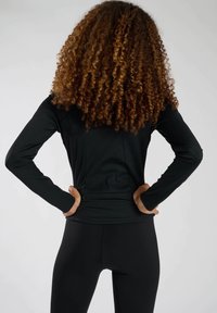 Czarna sportowa bluzka z długim rękawem o dopasowanym kroju, z teksturowanej tkaniny i dyskretną kieszonką na zamek z tyłu, w zestawie z czarnymi leginsami.