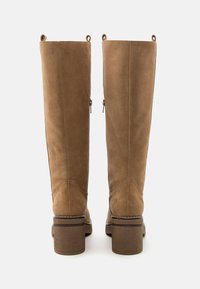Par de botas de ante marrón hasta la mitad de la pantorrilla con tacones cuadrados, vista trasera, mostrando la cremallera trasera y las pestañas de tirón sobre un fondo blanco.