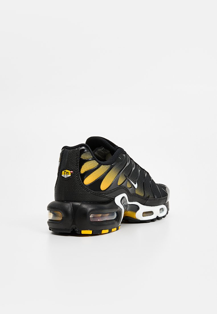 Schwarzer Laufschuh mit gelben Akzenten, strukturiertem Mesh-Obermaterial und Luftpolsterung. Verfügt über eine auffällige Markenkennzeichnung und ein einzigartiges wellenförmiges Design.