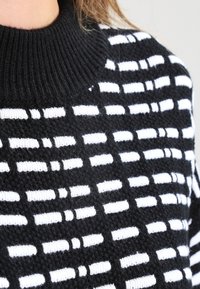 Czarnobiały sweter na drutach z fakturowanym wzorem poziomych pasków, ściągaczem przy dekolcie i miękkim materiałem.
