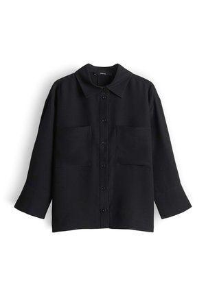 Schwarzes, langärmliges Hemd mit Knopfleiste, Kragen und zwei vorderen Brusttaschen, flach auf einem weißen Hintergrund liegend.