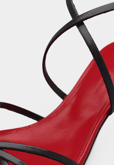 Κόκκινο σανδάλι με λεπτές μαύρες λουρίδες από δερμάτινο γυαλιστερό υλικό που διασταυρώνονται πάνω στη σόλα.