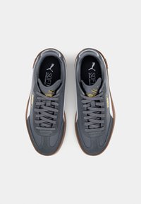 Grå sneakers med en slät läderöverdel, brun gummisula, snörningsdesign och gulddetaljer. Har "SOFT"-logotyp på innersulan.