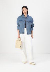 Veste en denim à coupe classique, avec deux poches avant, couleur bleu délavé, assortie à un pantalon large blanc et un mini cabas beige.