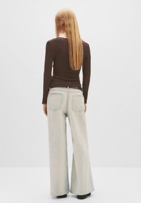 Brun, ribbet langærmet top parret med lyseblå, brede jeans. Jeansene har lommedetaljer og et let slidte look.