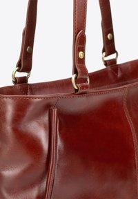 Brązowa skórzana torebka o gładkiej fakturze, z hardwarem w złotym kolorze i podwójnymi uchwytami. Posiada boczną kieszeń oraz starannie wykonane szwy.