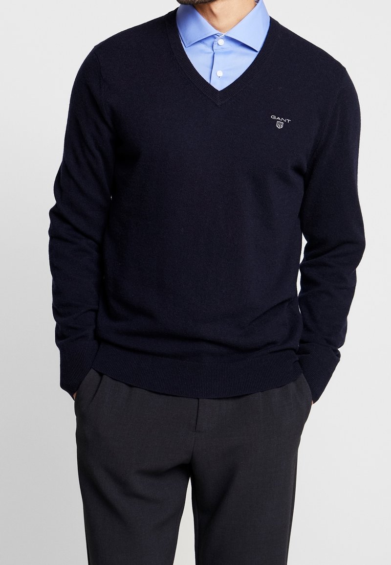 Marinblå V-halströja i mjukt stickat tyg, med ribbade ärmslut och nederkant, kombinerad med en ljusblå skjorta med krage under.