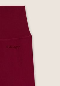 Sezione in tessuto a vita alta color bordeaux con logo "FREDDY" subtile in rilievo dello stesso colore su sfondo beige chiaro.