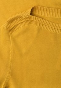 Gros plan d'un pull tricoté jaune montrant un col rond côtelé et des détails de coutures aux épaules sur un tissu lisse.