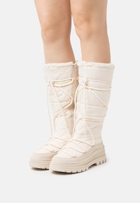 Knöchelhohe Winterstiefel in Creme, mit gestepptem Design, gefälschtem Futter an der Oberseite und weißen Schnürsenkeln sowie einer strapazierfähigen Gummisohle.