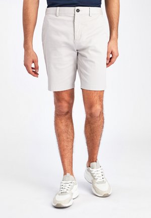 Light gray shorts made of cotton blend fabric with a button closure and two side pockets, paired with white and gray athletic shoes.