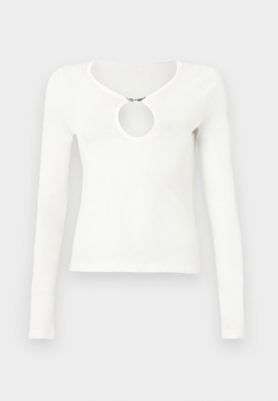 Άσπρο εφαρμοστό τοπ με μακριά μανίκια και στρογγυλή εσοχή στο στήθος που κλείνει με μικρό μεταλλικό κλιπ.